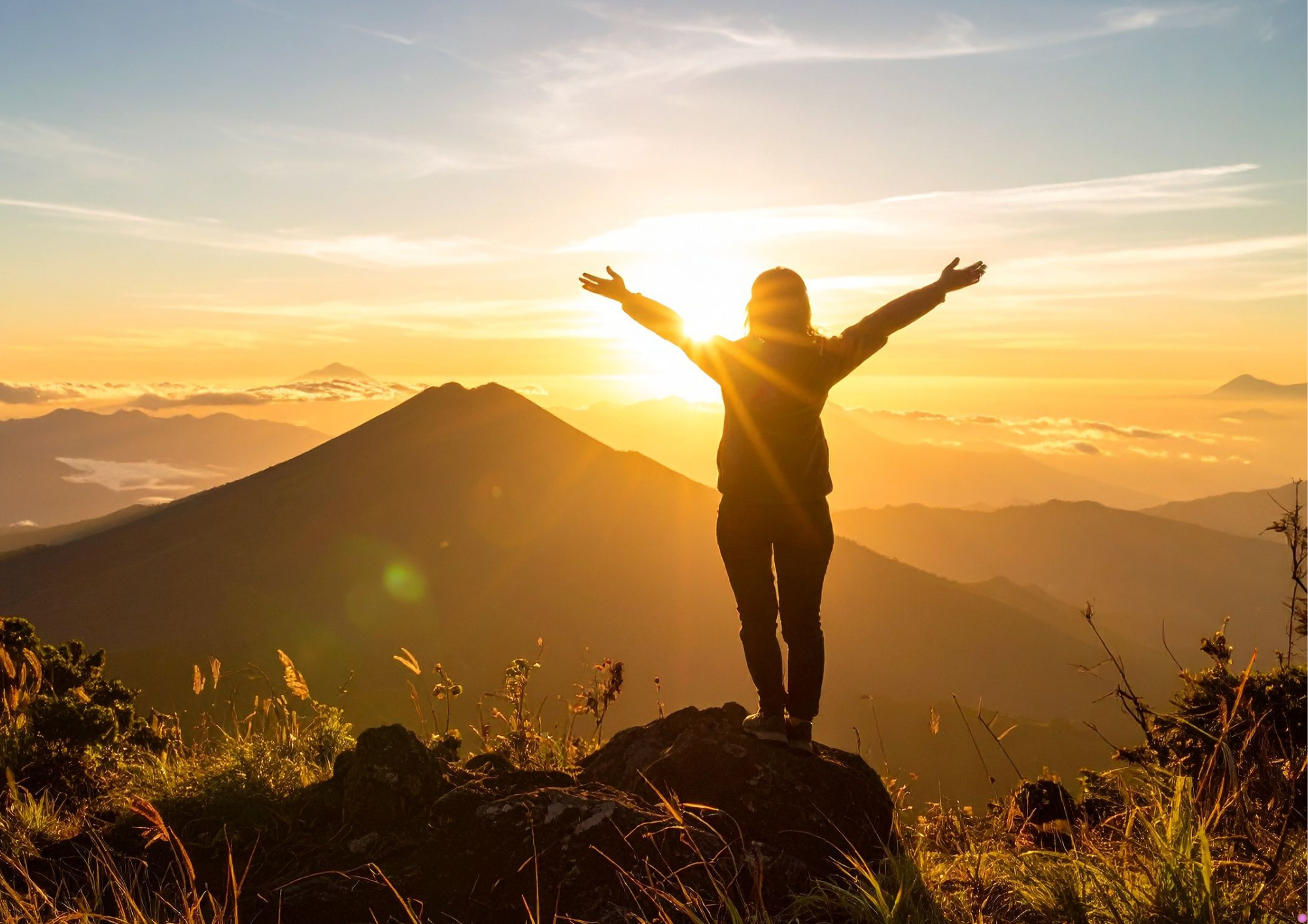 Frau auf Berggipfel schaut zur Sonne und hat ihr Trauma bewältigt
